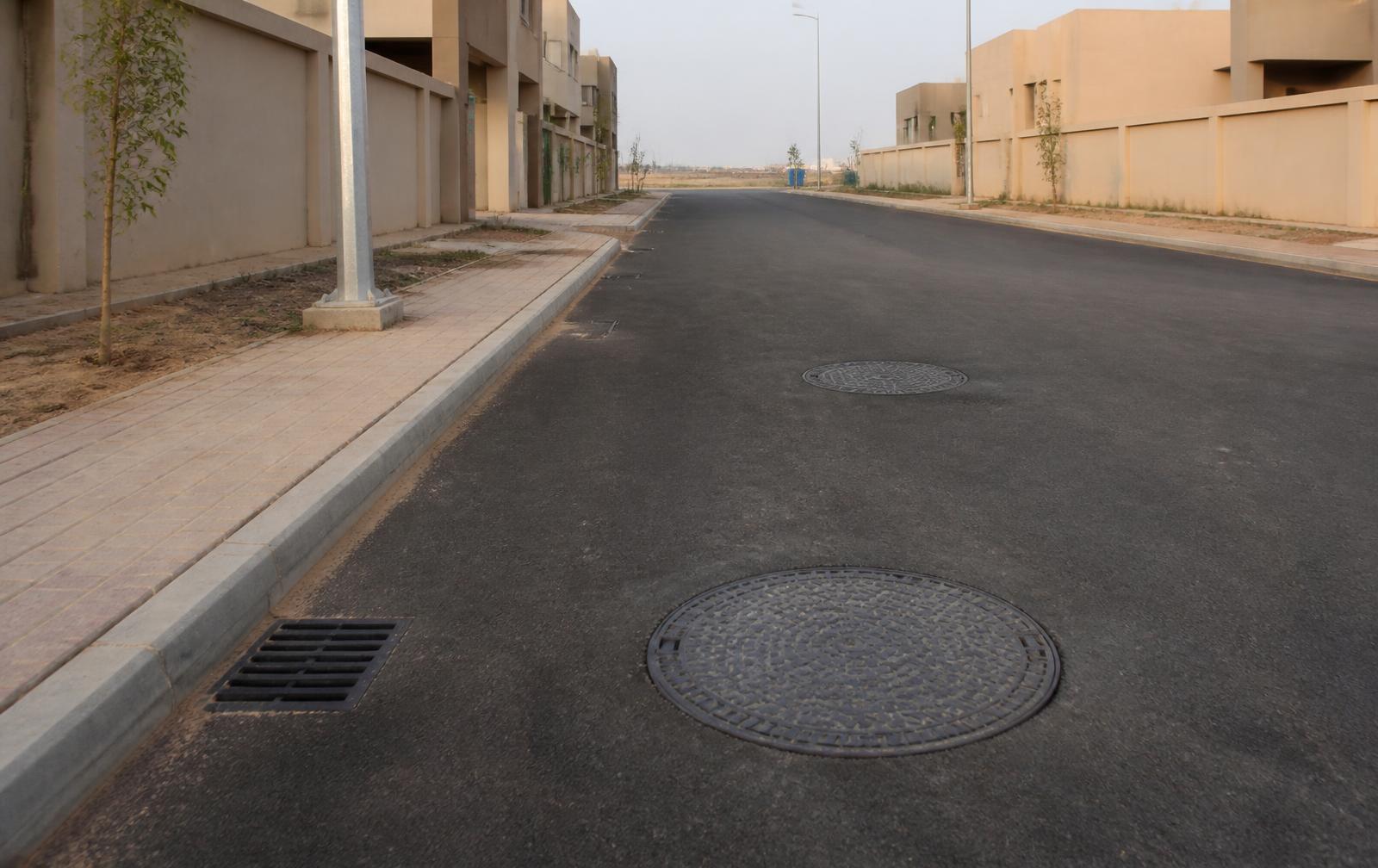 Ductile iron manhole cover and gully grating set into a new road in a Pakistani housing society